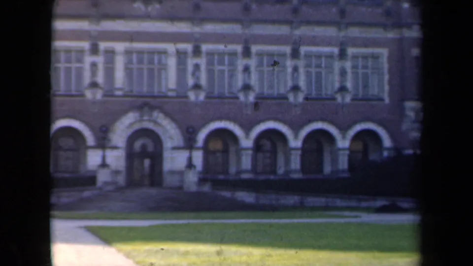 Soft 1946 Netherlands 8mm view of a historic-looking facade with arched doorways, rectangular upper windows, hedges, lawn, and paths.