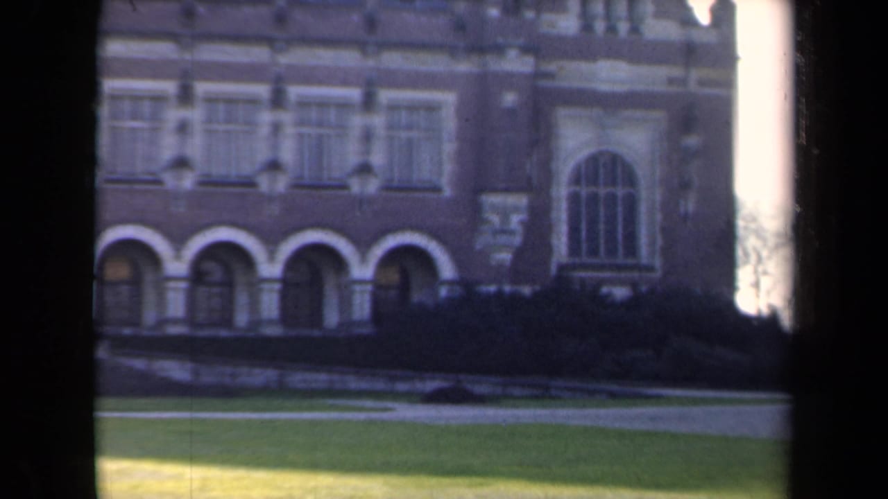 Similar facade view with arched entryways, tall window, lawn, shrub line, and film-edge border.