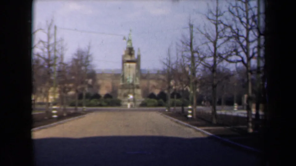 1946 Netherlands travel footage frames a tree-lined road and distant green-topped monument from a moving vehicle.