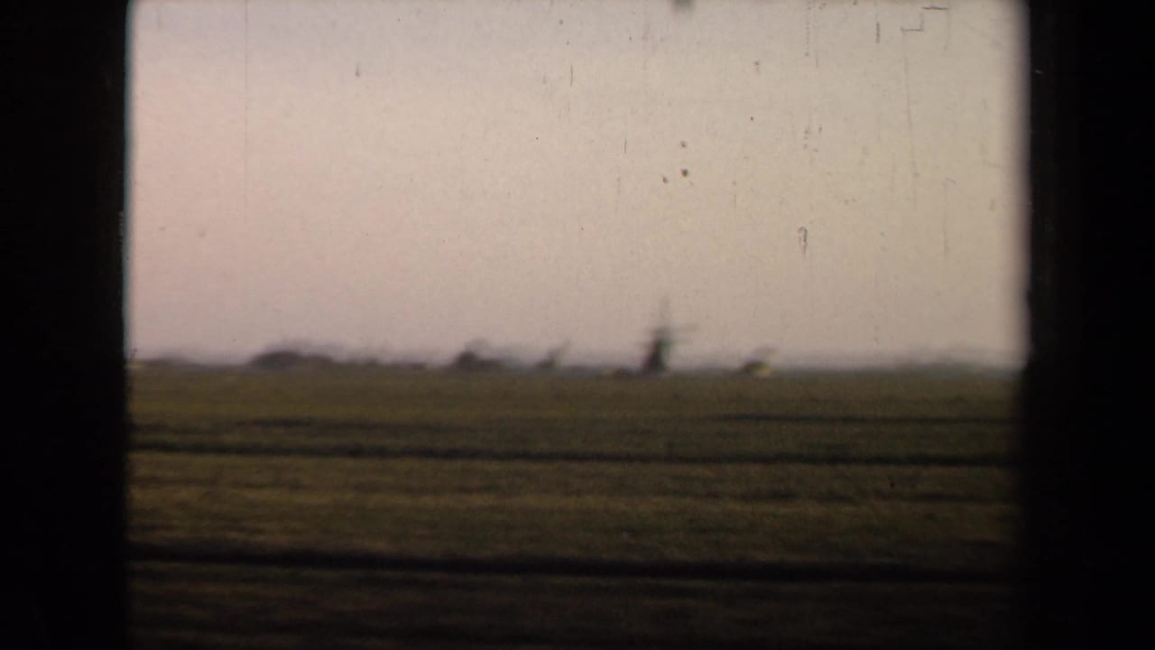 Rural fields and a distant windmill viewed from a train, bordered by dark frame edges.