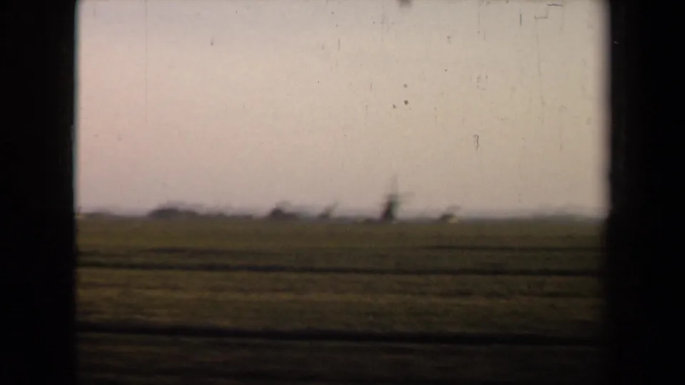 Soft 8mm view of Netherlands countryside from a train, with open fields, a pale sky, and a blurred windmill in the distance.