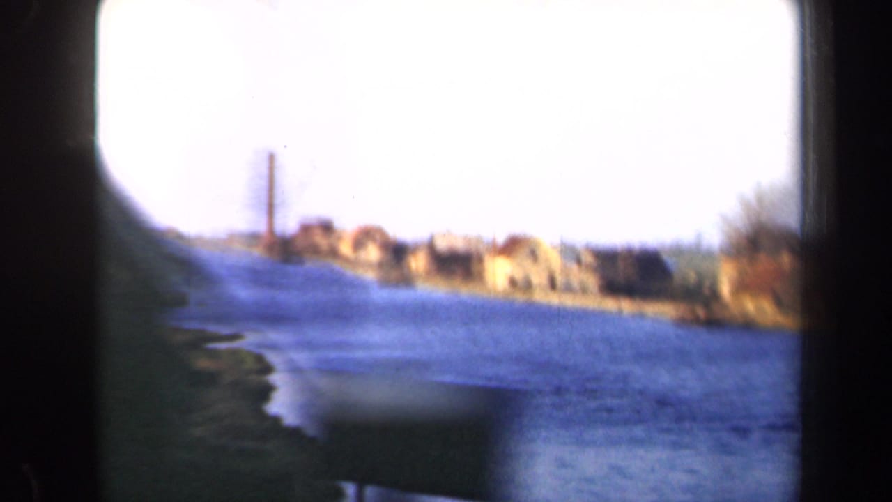 Bright overexposed view of a blue waterway with village buildings along the far bank.