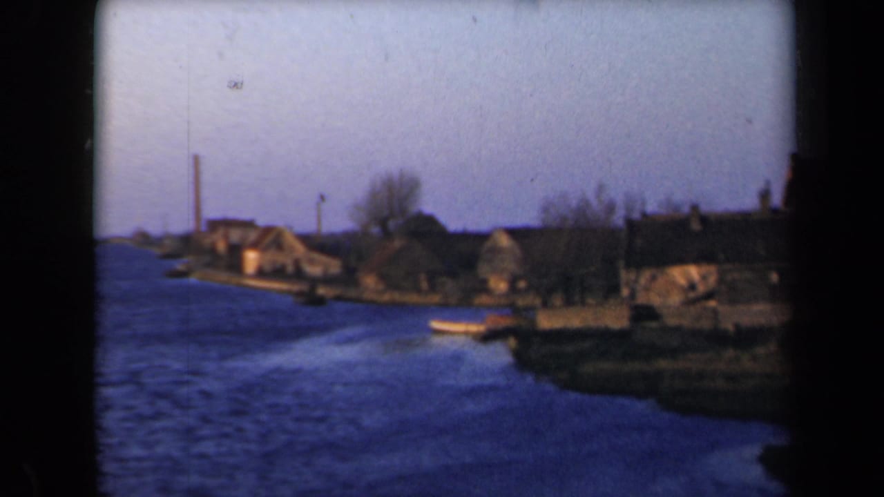 Waterway beside low houses and bare trees under a hazy sky.