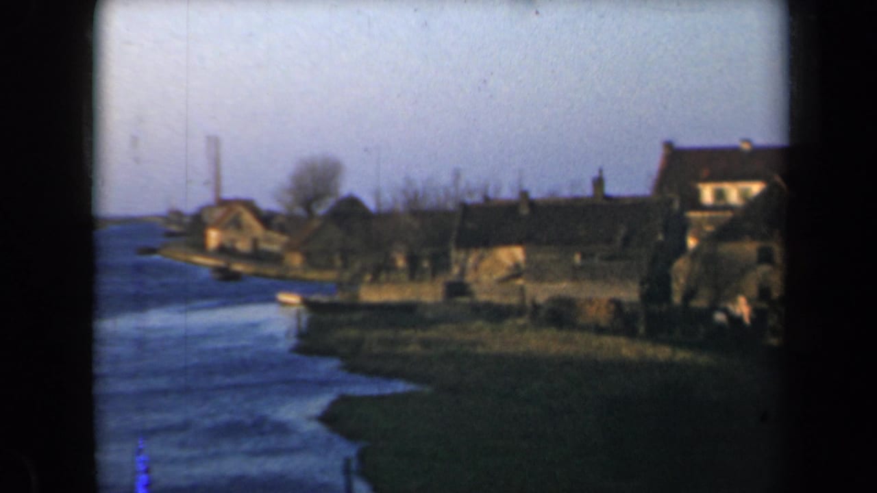 Riverside settlement with houses, grass bank, and water in the foreground.