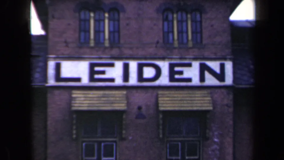 1946 Netherlands 8mm frame showing a brick facade with upper windows and a large white sign reading LEIDEN.