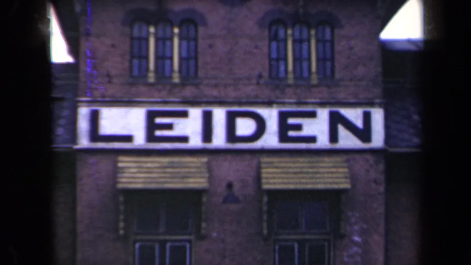 1946 Netherlands 8mm frame showing the LEIDEN sign centered on a brick building, with awnings, arched windows, and visible film-frame edge shadows.