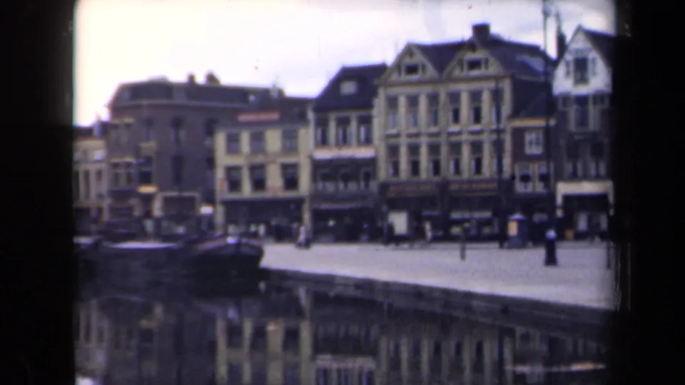 Dutch canal-town view from 1946 with multi-story gabled facades, pedestrians on the promenade, and a boat in the foreground.