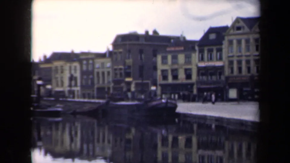 Soft 8mm view of a Dutch canal town in 1946, with pedestrians along the quay and reflected buildings in the water.