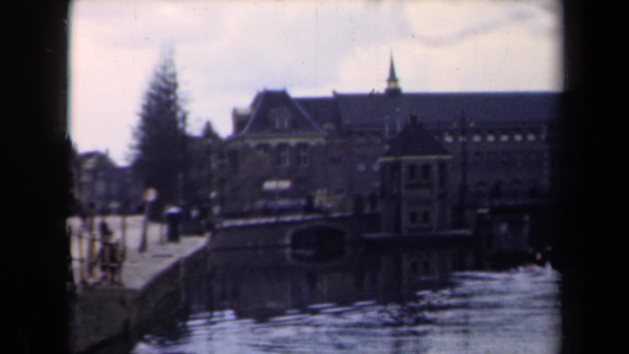 Canal beside a large brick building with pedestrians on the embankment.