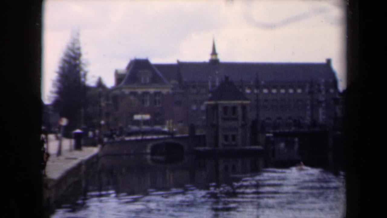 Waterfront building and canal with pedestrians near bicycles on the left quay.