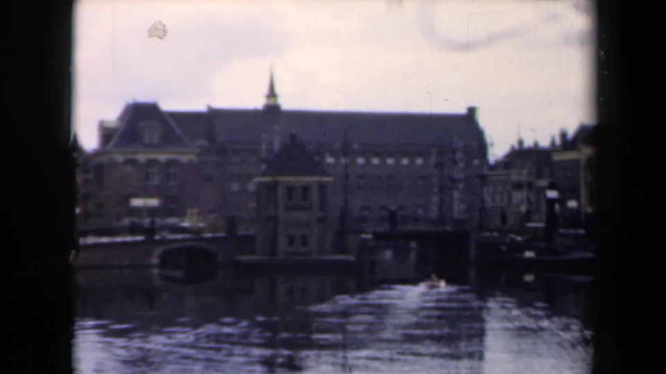 1946 Netherlands 8mm frame showing a canal bordered by historic buildings, with a spired roofline and dark reflections in the water.