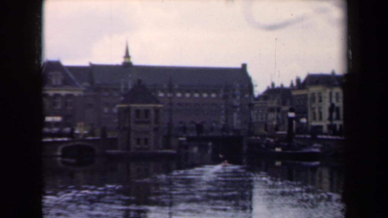 Waterfront buildings beside a canal with a small wake crossing the water.