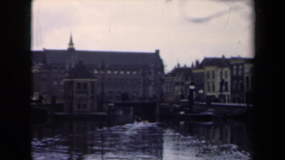 1946 Netherlands 8mm frame showing the pan across canal-side buildings, with a spire, gabled facades, and dark water reflections.