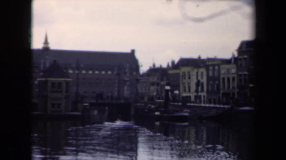 1946 Netherlands 8mm frame with canal water in the foreground, waterfront houses at right, and a large historic building behind them.