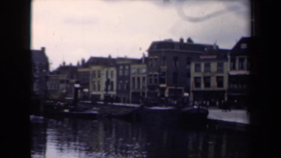 Dutch canal frontage in 1946 8mm footage, with traditional buildings and a dark boat at the quay.