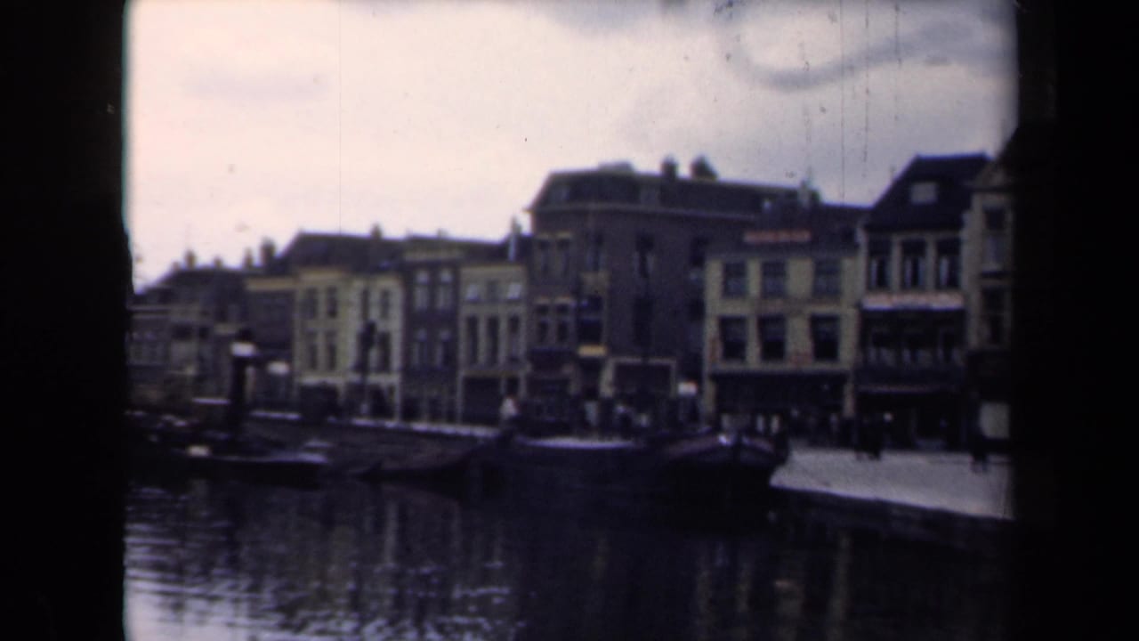 1946 home-movie view of a Dutch canal, moored boats, pedestrians, and gabled buildings along the quay.