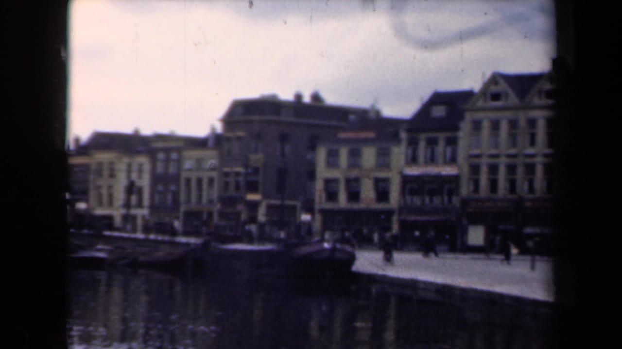 Waterfront street with boats, pedestrians, and rows of gabled buildings.