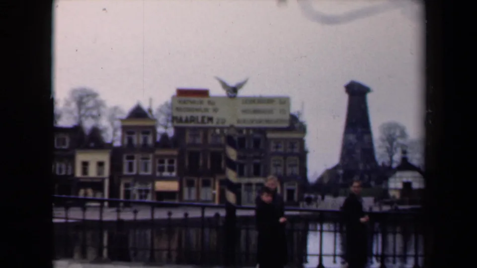 1946 Netherlands frame with a Haarlem 20 sign, canal railing, pedestrians, town buildings, and a dark tower beyond the water.