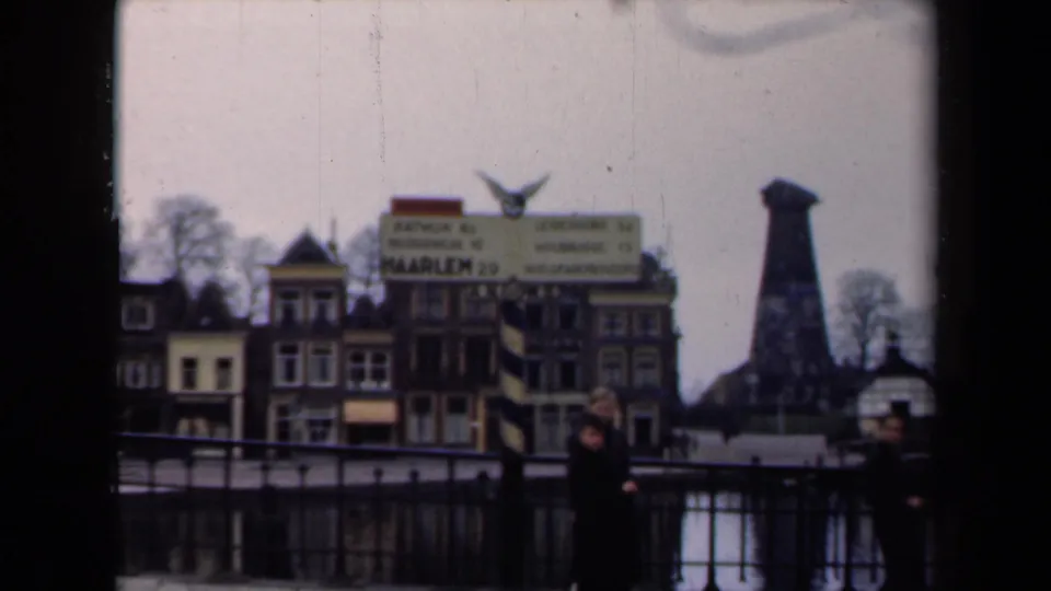 Home-movie frame from Haarlem, Netherlands, showing a canal railing, pedestrians, a large Haarlem 20 sign, and a tower in the background.