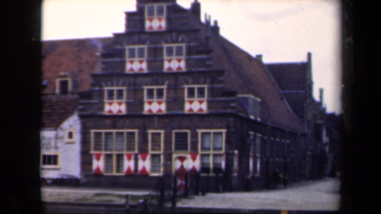 1946 Netherlands home-movie frame showing a stepped-gable building with patterned shutters and a side street.