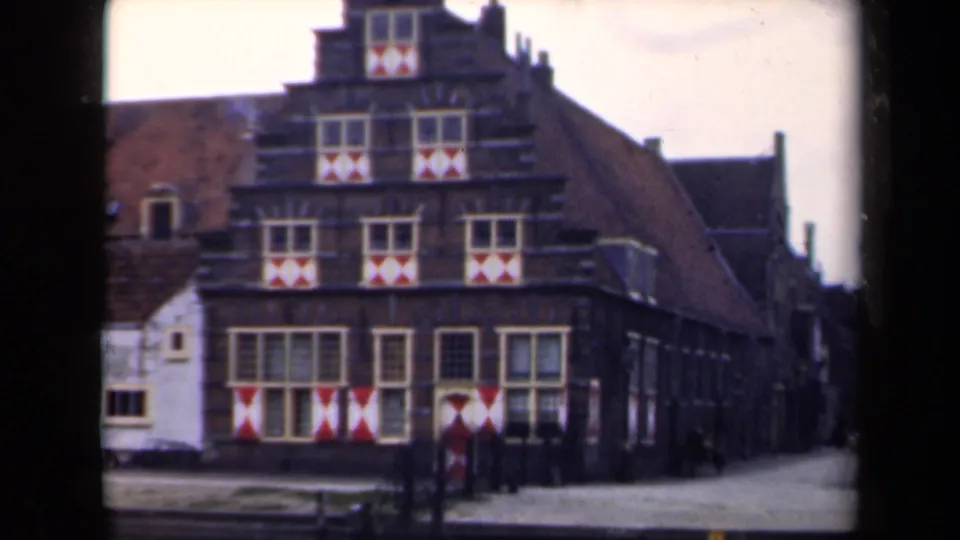 1946 Netherlands home-movie frame showing a stepped-gable building with patterned shutters and a side street.