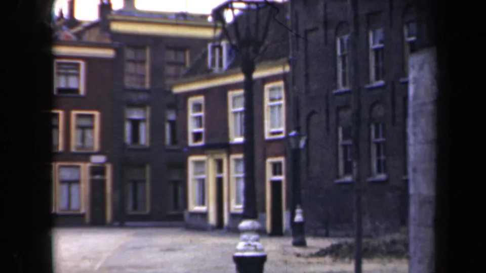 1946 Netherlands street view with closely spaced brick buildings, many windows, shutters, bare trees, and a black lamppost in the foreground.