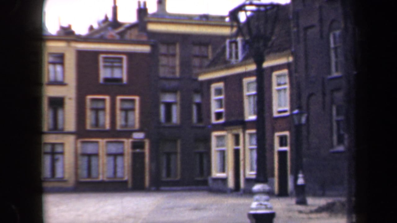 1946 Netherlands 8mm frame showing a quiet street lined with narrow Dutch townhouses, multi-paned windows and a lamppost.