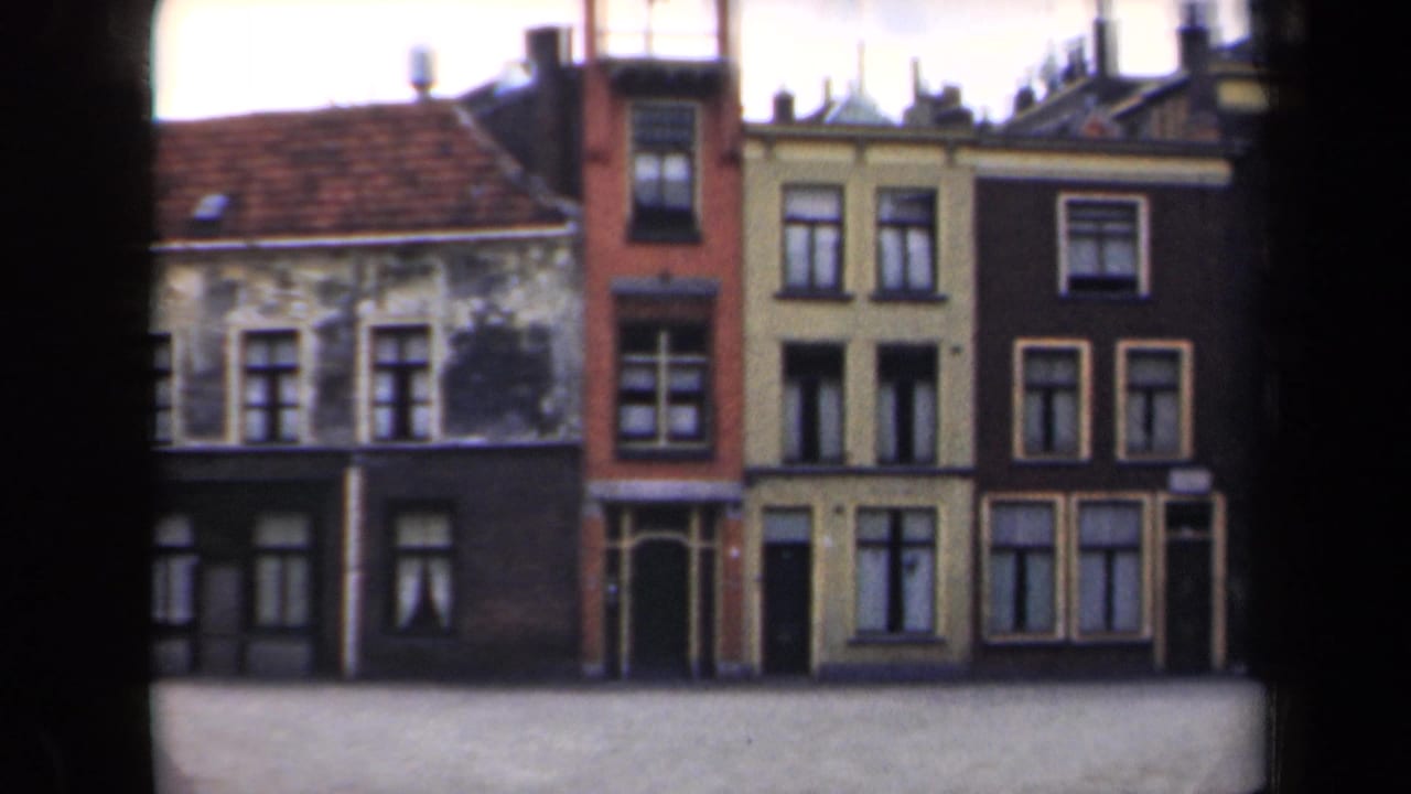 1946 Netherlands 8mm frame showing attached town buildings with weathered facades, tiled roofs, and a quiet open street area.