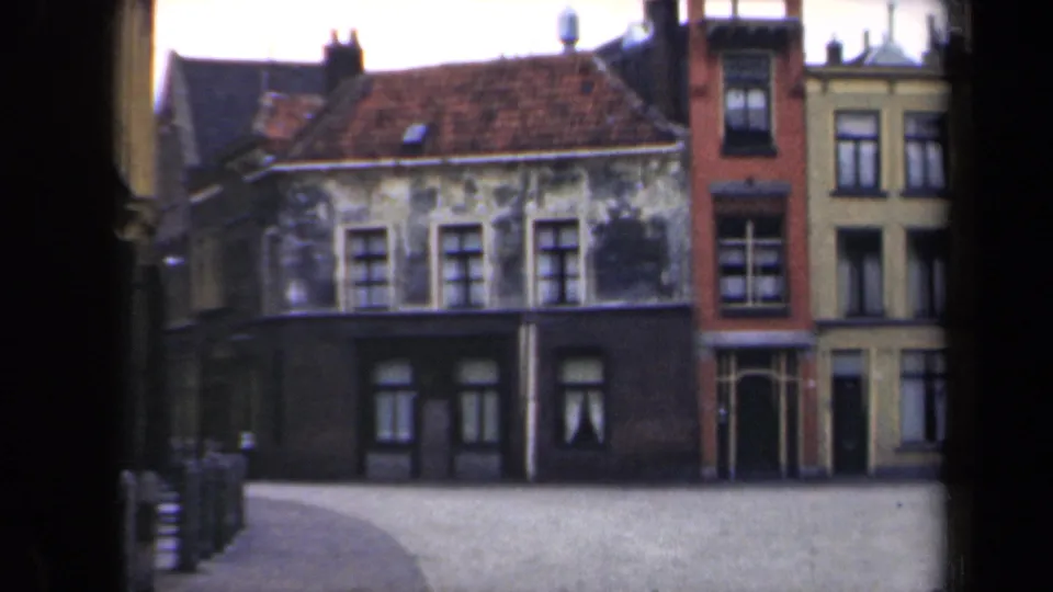 1946 Netherlands 8mm view of older connected buildings with worn plaster, dark lower storefronts, and a gently curving paved street.