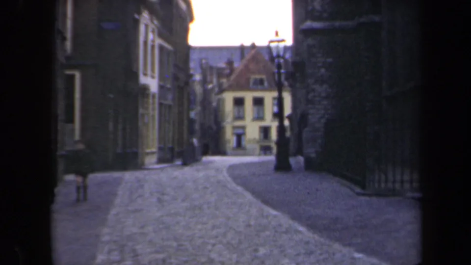 1946 Netherlands street scene showing cobblestones, historic buildings, an old lamppost, and a distant passerby in the roadway.
