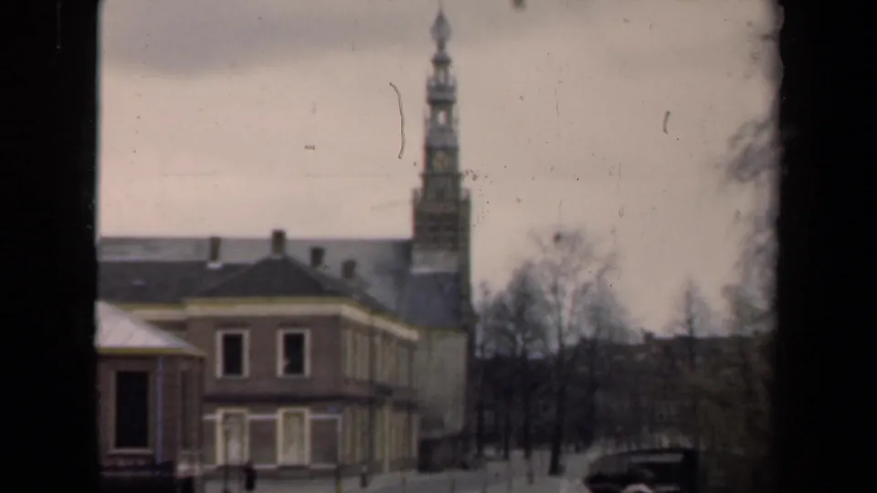 1946 Netherlands home-movie frame showing the canal-side building, tower, bare trees, and dark car under an overcast sky.