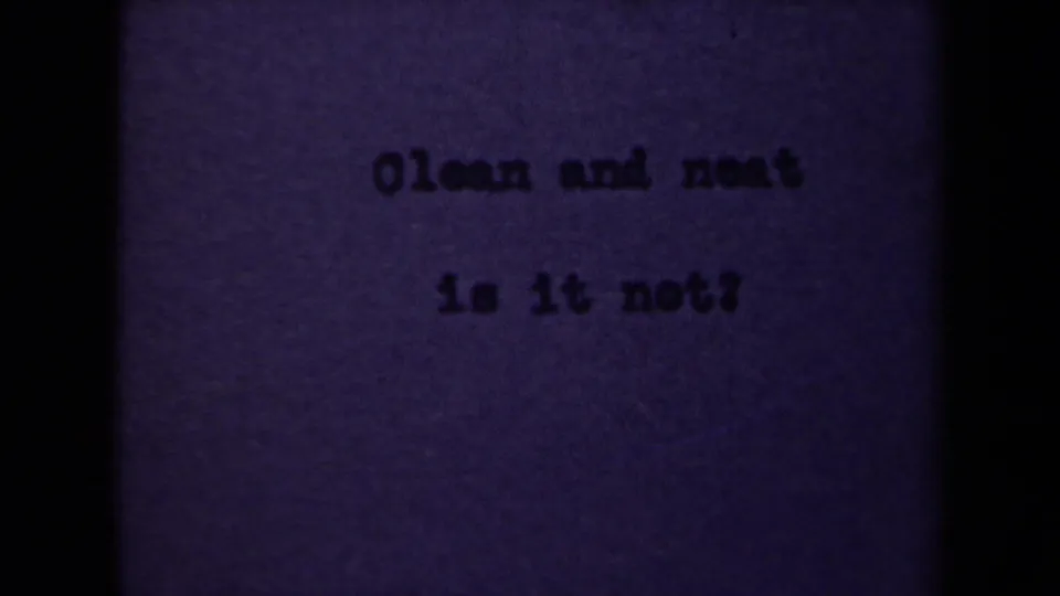 1946 Netherlands 8mm frame showing the typed phrase Clean and neat is it not? on purple-tinted paper with dark gate edges.