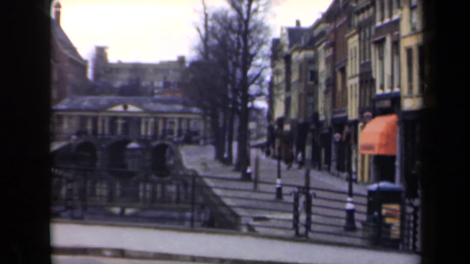 1946 Netherlands home-movie view of canal-side railings, steps, bare trees, narrow buildings, and an orange shop awning.