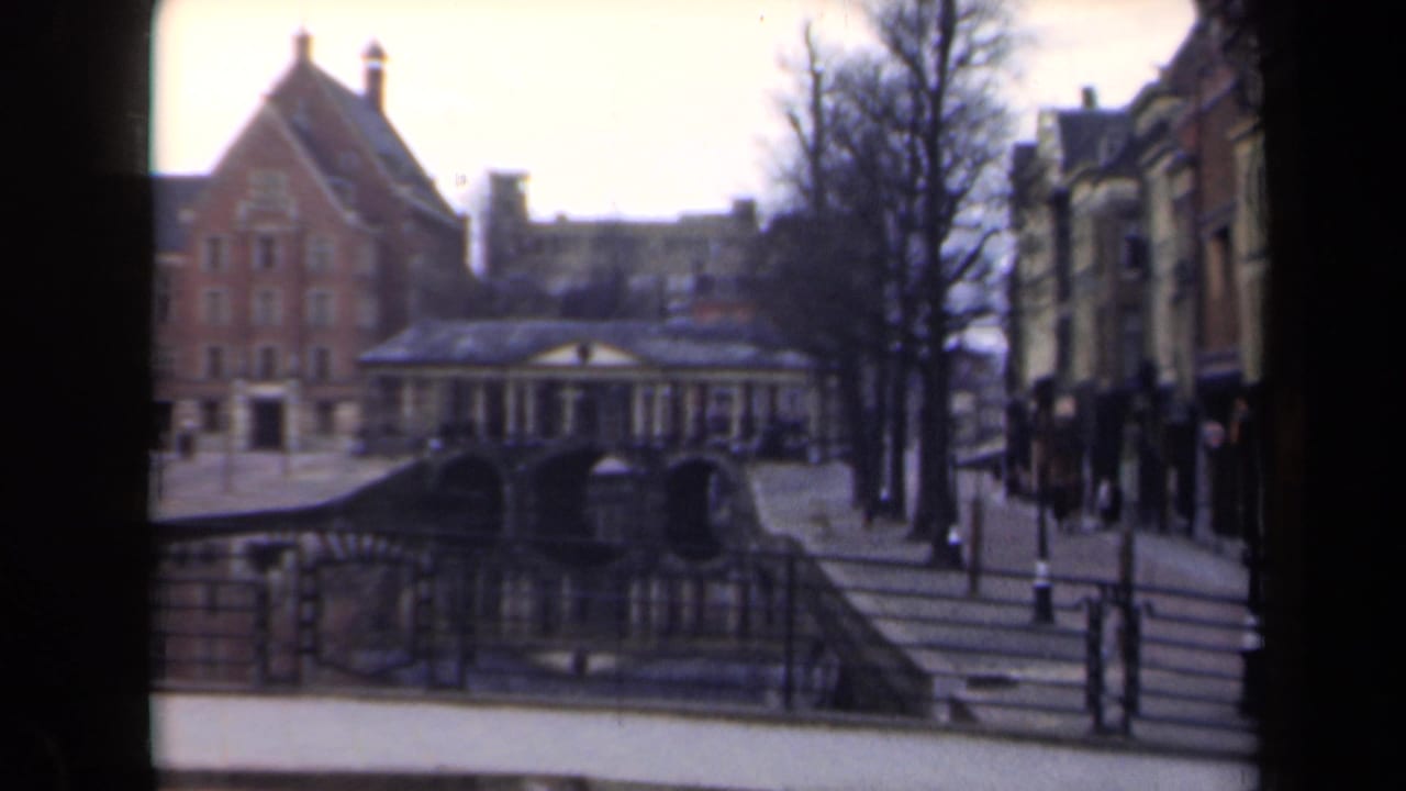 1946 Netherlands 8mm frame showing a canal, arched bridge, brick architecture, bare trees, railings, and distant pedestrians.