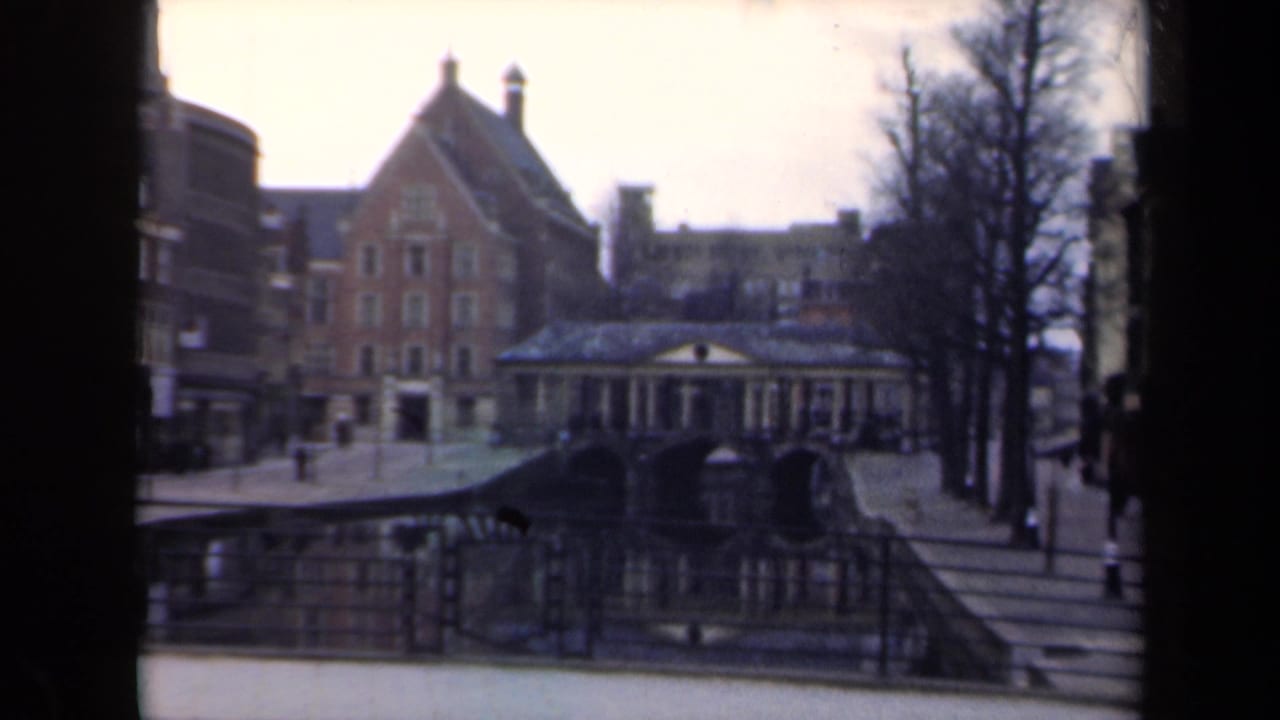 Canal bridge and brick buildings viewed through a dark film-frame border, with pedestrians nearby.