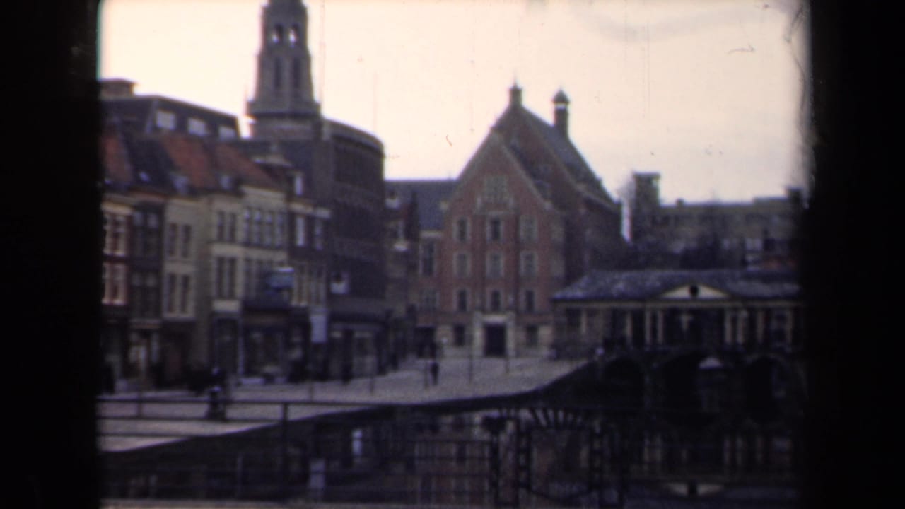 1946 Netherlands 8mm frame showing a quiet street with gabled buildings, a tall tower, pedestrians, and a distant scooter.