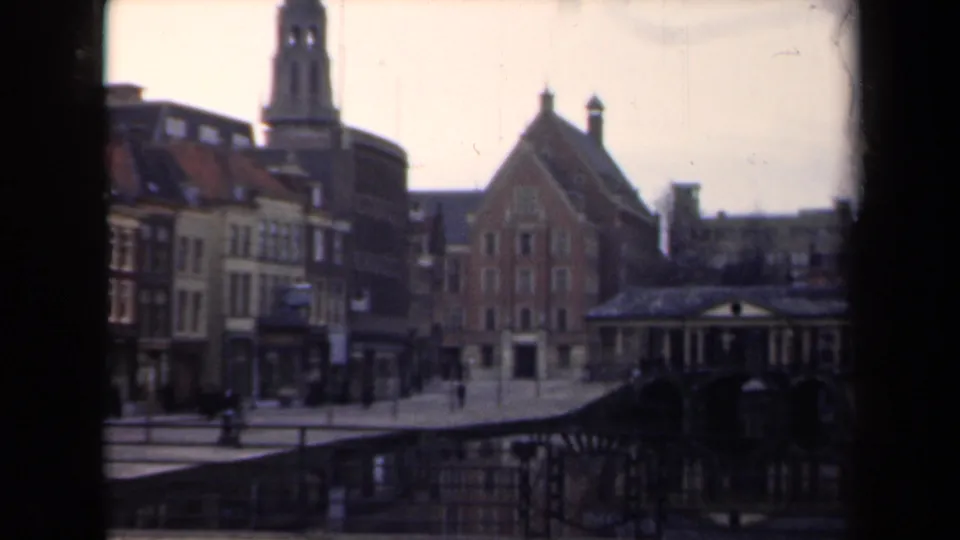 1946 Netherlands 8mm frame showing a quiet street with gabled buildings, a tall tower, pedestrians, and a distant scooter.