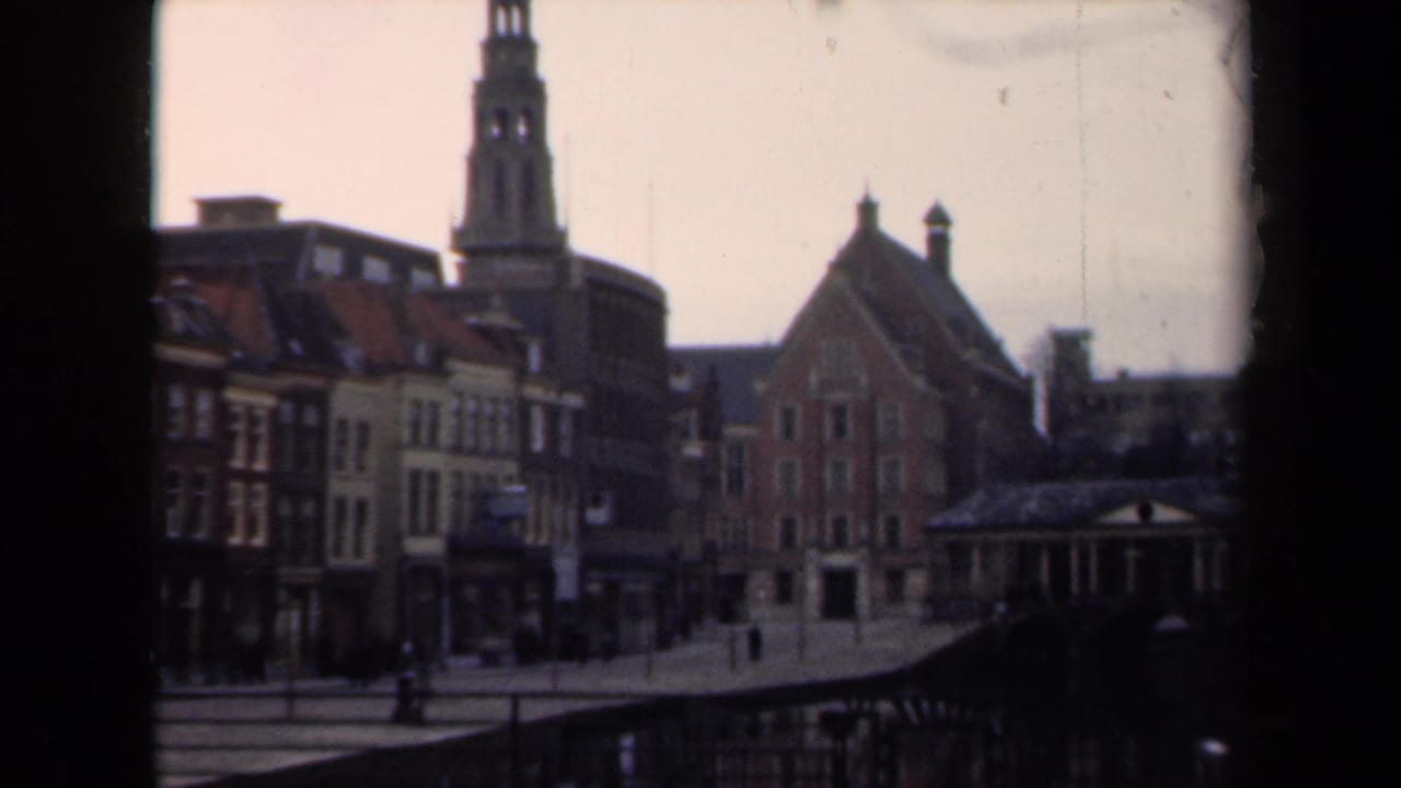 1946 Netherlands street view with traditional gabled buildings, a tower rising behind them, and small pedestrians along the roadway.