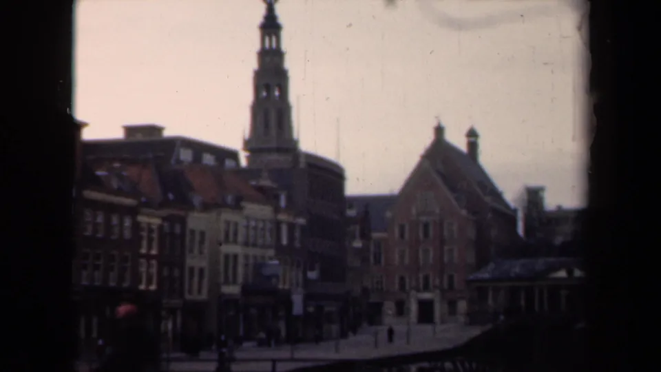 1946 Netherlands 8mm frame with a closer view of brick and stucco buildings, a tower, sparse pedestrians, and soft muted color.