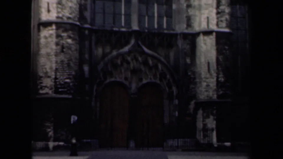 1946 Netherlands frame showing a dark gothic-style stone facade with large arched wooden doors and a small parking sign.