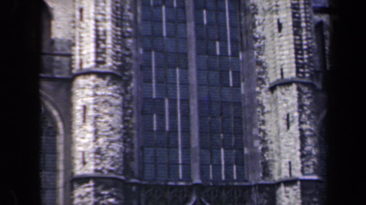 Close side view of a Gothic stone façade with tall dark windows and vertical masonry details.