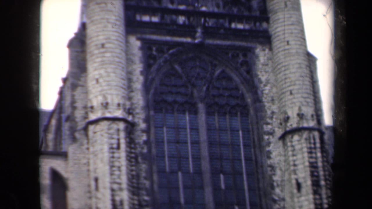 1946 Netherlands home-movie frame showing a close exterior view of Gothic stonework, arched windows, and cylindrical church towers.
