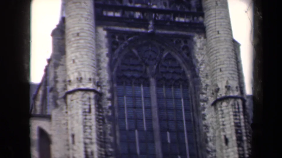 1946 Netherlands home-movie frame showing a close exterior view of Gothic stonework, arched windows, and cylindrical church towers.