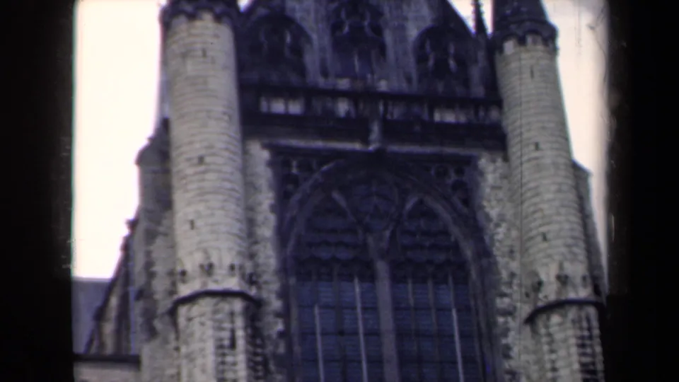 Close 8mm view of a Netherlands church exterior, with round towers flanking dark Gothic window tracery.