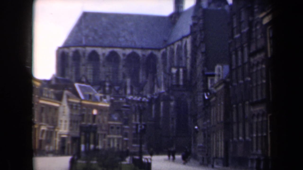 Large church and narrow street bordered by older buildings, with small pedestrians in the distance.