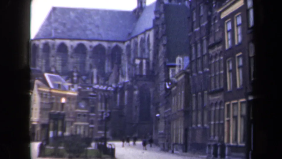 1946 Netherlands view of a Gothic church framed by older street buildings, with distant pedestrians and visible 8mm frame edges.
