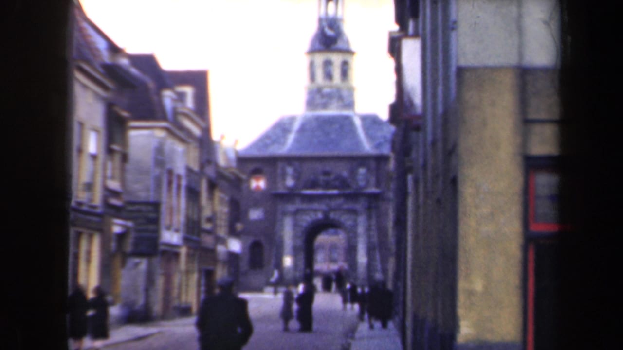 1946 Netherlands street view with pedestrians moving toward a historic stone gatehouse and tower between older building fronts.