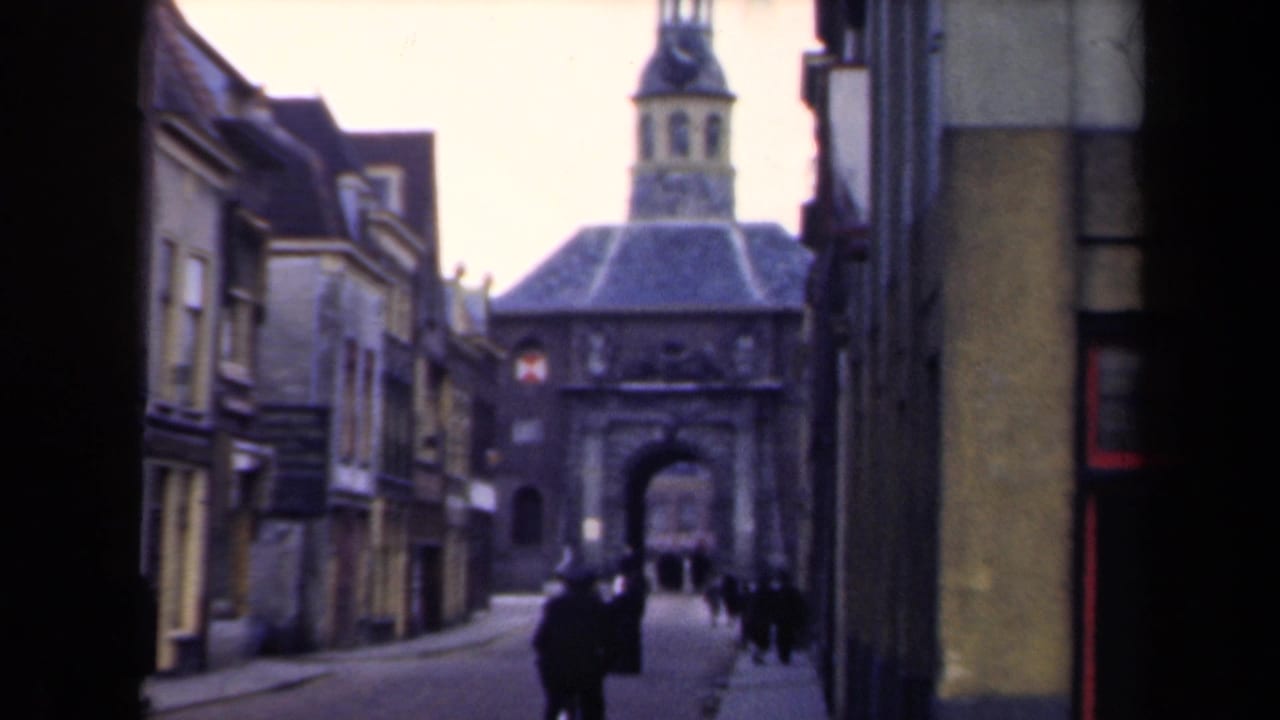 Pedestrians pass through a narrow street framed by buildings and a distant arched gate.
