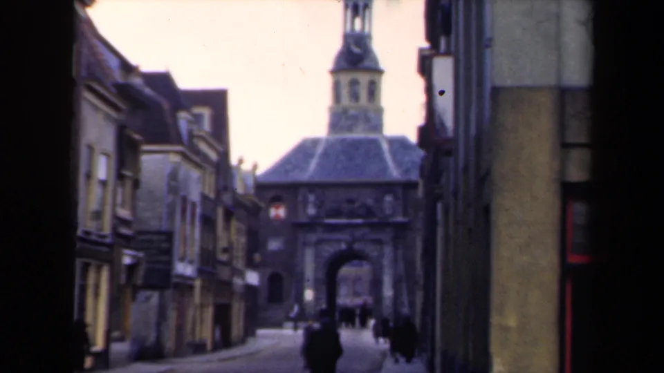 1946 Netherlands view down a narrow urban street toward a stone gatehouse, with pedestrians dispersed along the walkway.