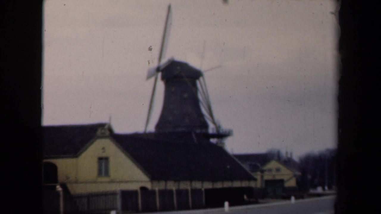 Large windmill beside a quiet road and low traditional buildings under an overcast sky.